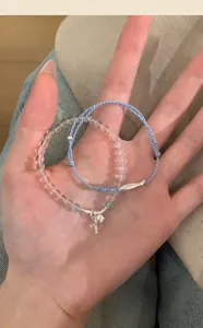 Macro view of clear stone beaded bracelet and blue braided cord bracelet with fish charm