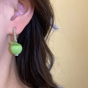 Detailansicht eines grünen Apfel-Anhängers am Ohr für einen frischen Sommer-Look