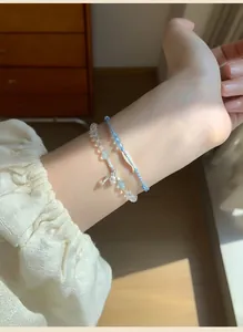 Close-up of beaded and woven cord bracelets with a fish charm on a model's wrist