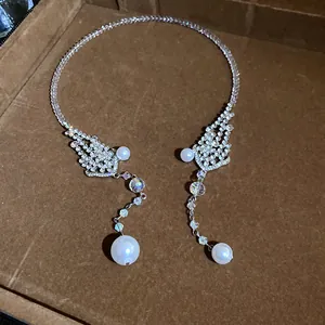 Detail view of an elegant rhinestone choker with pearl pendants on a brown velvet tray.