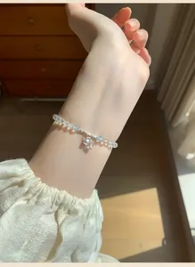 Close-up view of a minimalist stone beaded bracelet with a silver fish pendant on wrist.