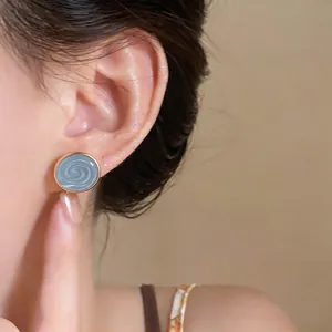 Macro view of a blue swirled enamel earring worn on a model's ear with gold trim.
