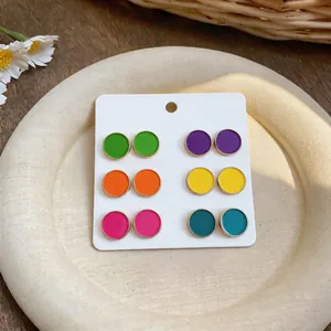 Detail view of six pairs of colorful enamel round stud earrings on a white display card.