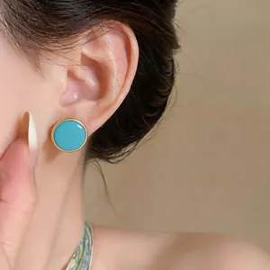 Close-up detail of a turquoise blue enamel stud earring with a gold rim