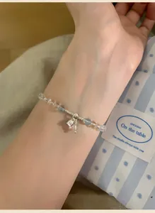 Detailed view of minimalist clear stone beaded bracelet with bell pendant on model's wrist