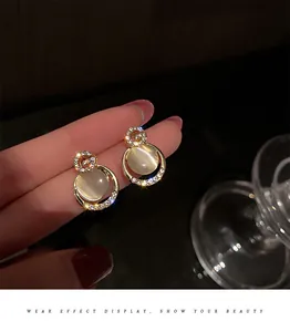 Close-up detail of cat-eye stone earrings with rhinestone encrusted G-letter design