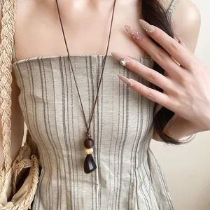 Gros plan d'un collier avec pendentif en résine et bois sur une robe en lin rayée.