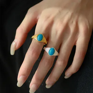 Elegante goldene und silberne Ringe mit ovalem Türkis auf dunklem Hintergrund getragen.
