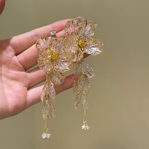 Close-up of acrylic flower tassel earrings with golden edges held by hand