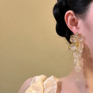 Exquisite gold-toned acrylic flower tassel earrings worn by a model in a warm setting