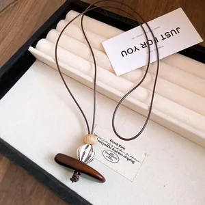 Gros plan d'un collier avec pendentif en résine et bois sur un plateau à bijoux beige.
