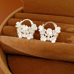Close-up detail of silver flower basket hoop earrings with white shells and pearls.