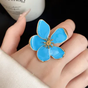 Close-up detail of oversized light blue enamel flower open ring worn on hand with gold edge