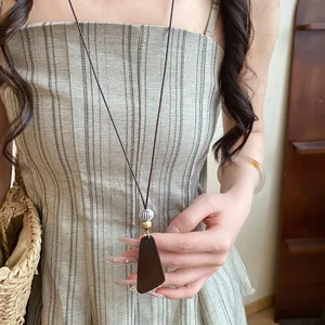 Gros plan d'un long collier en cordon de cuir avec un pendentif en résine effet bois sombre
