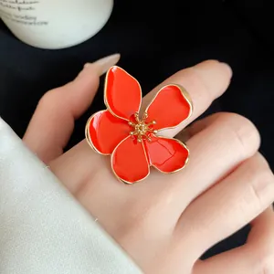 Detailed view of an oversized red enamel flower ring with gold trim on a finger