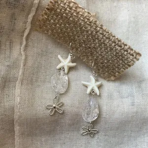 Dettaglio di orecchini a stella marina con perle trasparenti e ciondoli argentati.