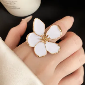 Detailed macro view of a large white enamel flower ring with golden trim worn on a finger