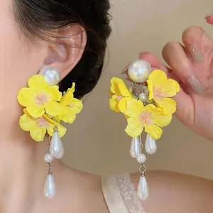 Detail of yellow fabric flower earrings with teardrop pearl tassels on a model