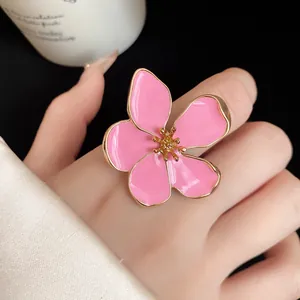 Detailed macro view of an oversized pink enamel flower ring on finger with gold plating