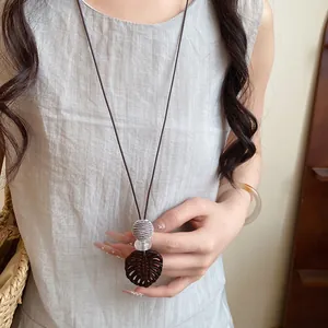 Vue détaillée d'un collier avec pendentif feuille et perles en résine sur cordon.