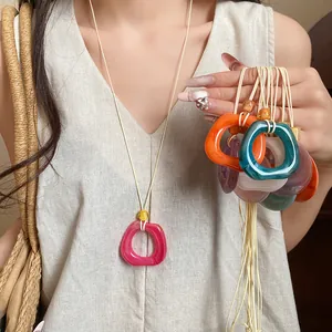 Close-up detail of various colorful resin geometric ring necklaces on a minimalist cord.