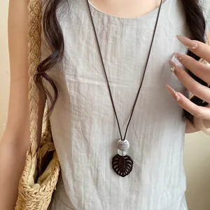 Vue détaillée d'un collier long en cordon de cuir avec un pendentif feuille de monstera