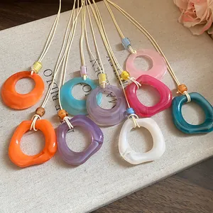 Variety of colorful resin ring necklaces with cord strings on a vintage book background.