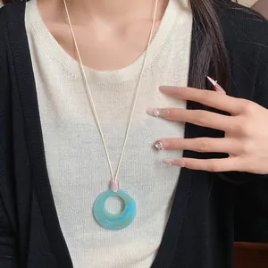 Close-up of a stylish blue resin ring pendant necklace worn over a white knit top