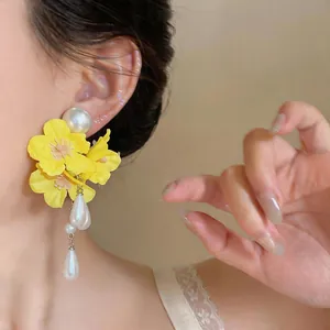 Detailed view of yellow fabric flower earrings with elegant pearl teardrop tassels.