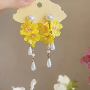 Detailed macro view of yellow fabric flower earrings featuring elegant white pearl tassels