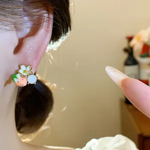 Primo piano dei dolci orecchini a forma di fragola e fiore placcati in oro.