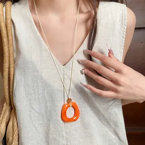 Close-up of a model wearing an orange geometric resin ring necklace on a cream linen vest.
