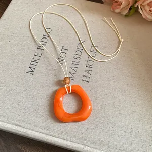 Close-up of an orange resin ring pendant on a minimalist cream cord necklace detail