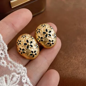 Macro view of vintage oval gold-toned stud earrings featuring intricate black enamel flowers