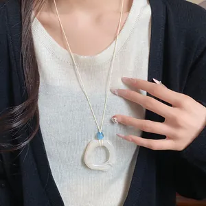Close-up of minimalist resin ring pendant necklace on white cord, worn over knitwear.