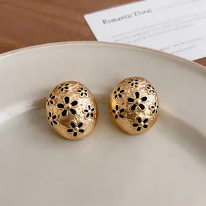 Macro detail of vintage gold oval stud earrings featuring black oil enamel floral motifs