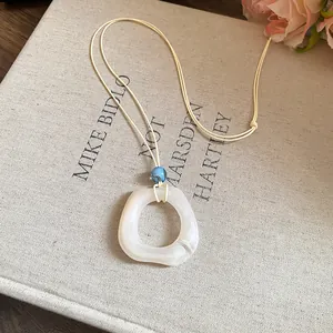 Detail of a minimalist resin ring pendant necklace on a cream cord with blue bead