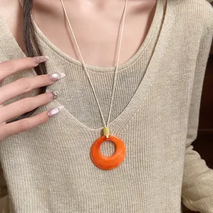 Macro view of an orange resin ring pendant necklace on a beige knitted sweater model