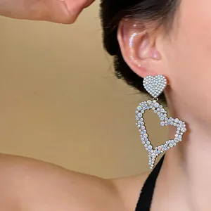 Close-up of sparkling heart-shaped drop earrings with rhinestone details on a model