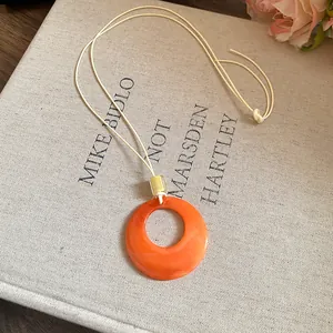 Close-up detail of a minimalist orange resin ring pendant necklace placed on a vintage book