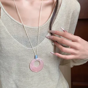 Minimalist pink resin circular ring necklace with long cord, worn on beige knit top.
