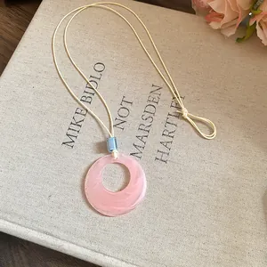 Close-up detail of pink resin ring necklace with blue bead on canvas book background