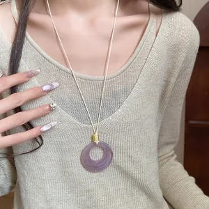 Detail shot of a minimalist purple resin ring necklace worn with a beige sweater