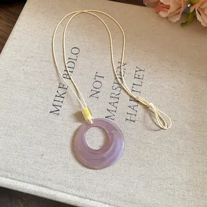 Detail view of a purple resin ring pendant on a minimalist beige cord necklace.
