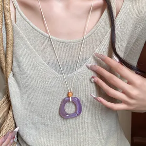 Detail of purple resin ring necklace worn on a beige knit top for a retro look.