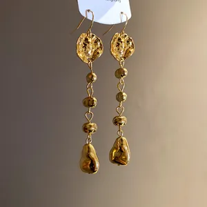 Gros plan de boucles d'oreilles pendantes à pampilles dorées avec texture martelée vintage