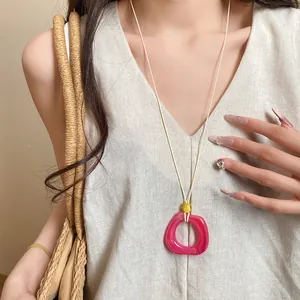 Close-up of a vibrant fuchsia resin ring pendant on a minimalist cream cord necklace
