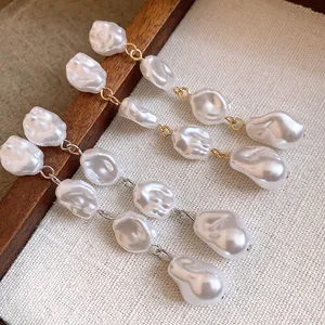 Dettaglio macro di orecchini a nappa con perle barocche irregolari in finitura oro e argento.