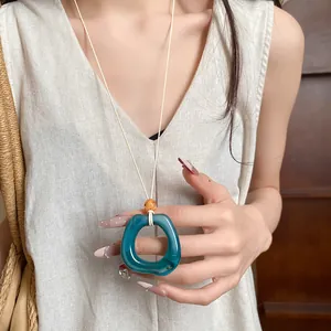 Close-up detail of a retro blue resin ring pendant necklace styled on a linen dress