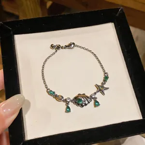 Close-up detail of shell and starfish charm bracelet with green emerald zircons